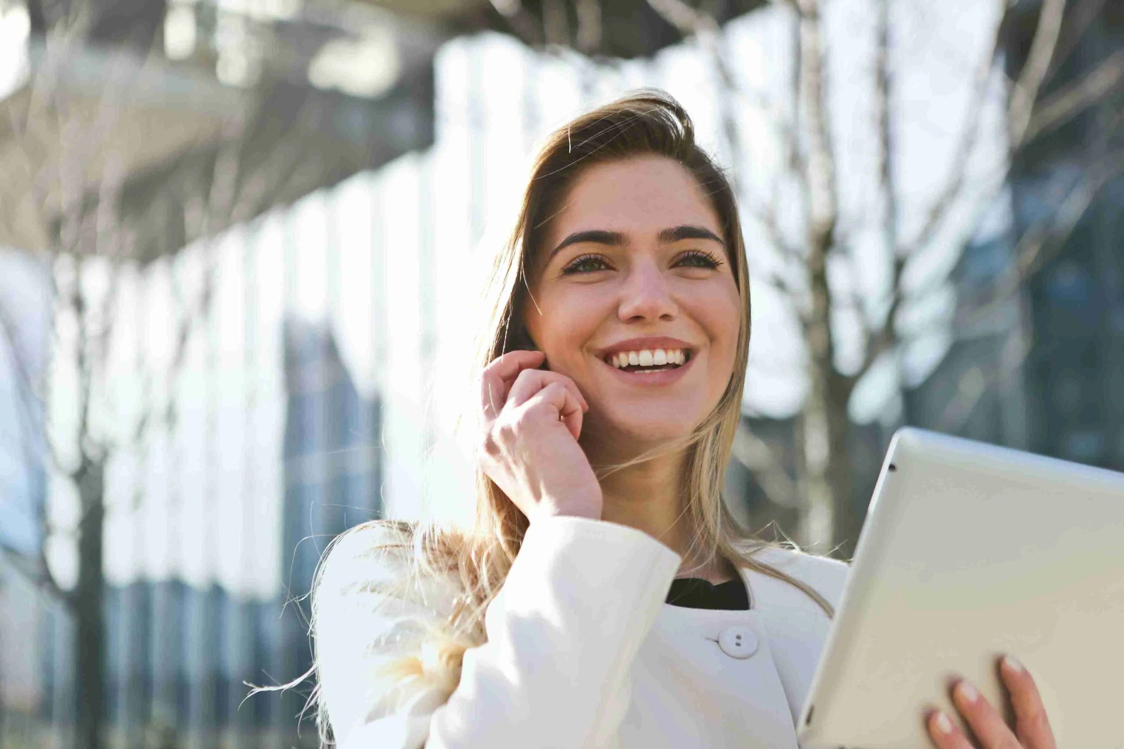 Mujer vestida formalmente sonriendo mientras habla por teléfono y sostiene una laptop